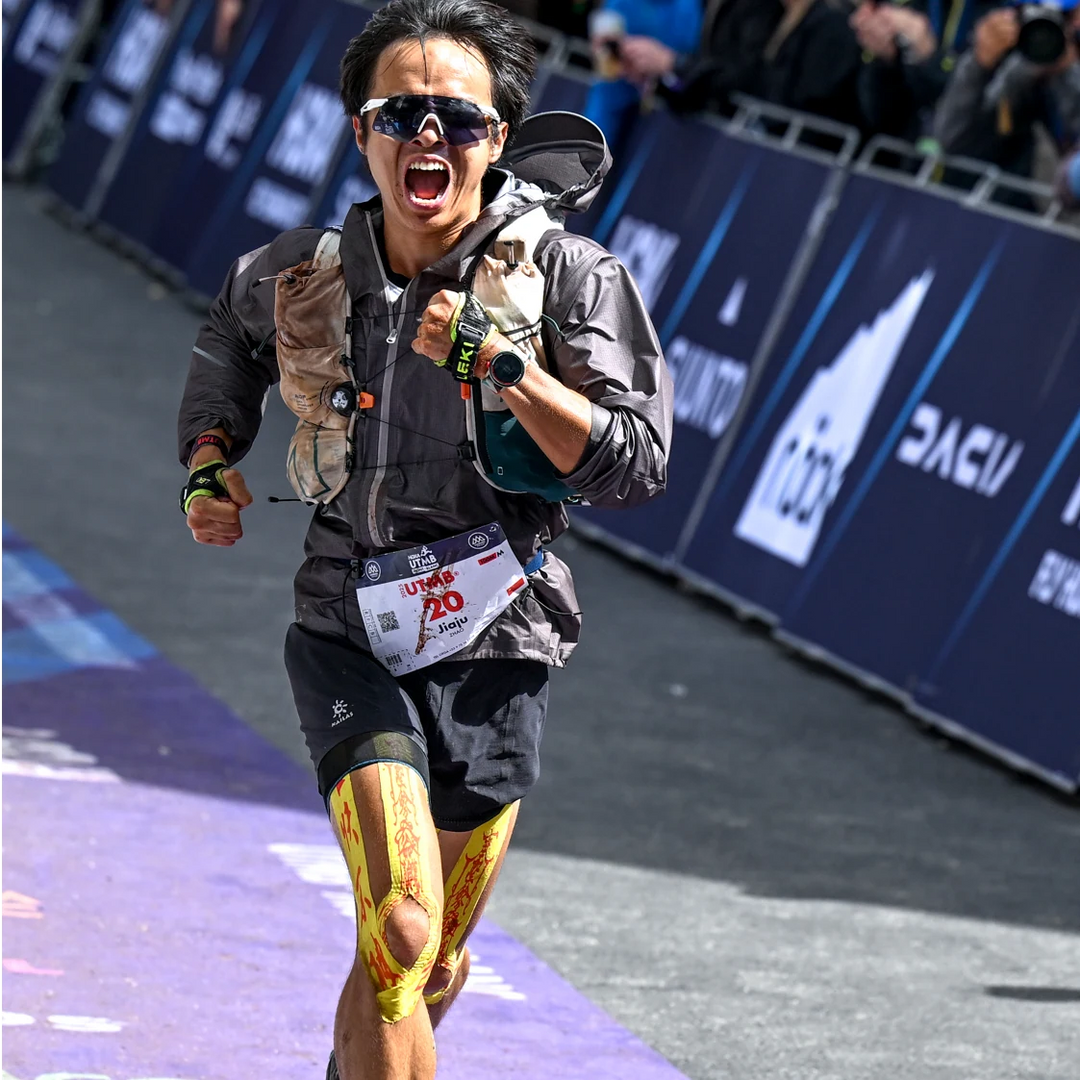 Ultrarunner crossing a mountain race finish line with yellow talisman tape on both legs